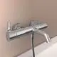 Einfache chromfarbene Badewannenarmatur von Ideal Standard mit integriertem Handbrauseschlauch und Wandhalterung, montiert an einer hellen Wand.